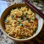 Close-up of a bowl of 3-Ingredient Ramen Stir-Fry with chopsticks, garnished with herbs and sesame seeds.