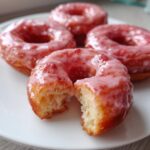 Close-up of air fryer mini donuts with strawberry glaze, one broken open to show texture.