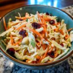 A bowl of fresh Apple Cranberry Coleslaw with shredded cabbage, carrots, apples, and cranberries.