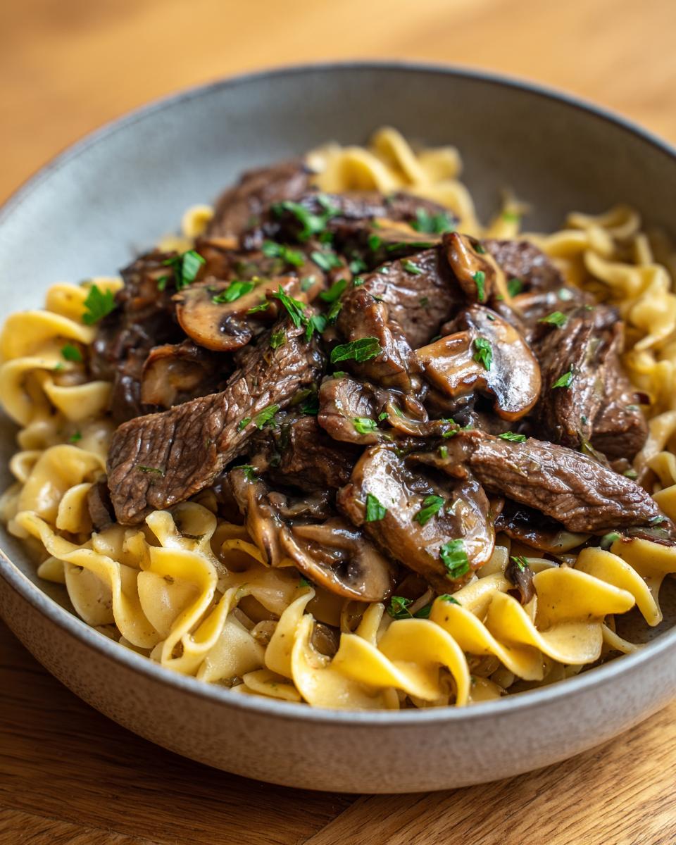 Close-up of Classic Beef Stroganoff with Egg Noodles in a bowl, showing beef, mushrooms, and noodles.