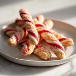 A pile of festive candy cane cookies, twisted and sprinkled with red sugar, ready for Christmas.