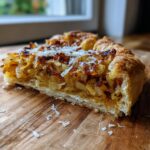 Close-up of a slice of Caramelized Onion Tart on a wooden surface, showing the caramelized onions and crust.