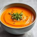 Close-up of a bowl of Carrot Ginger Detox Soup, garnished with fresh herbs.
