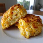 Close-up of freshly baked Cheddar Biscuits, golden brown and cheesy, on a white plate.