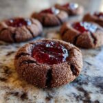 Close-up of a delicious chocolate thumbprint cookie filled with glistening raspberry jam.