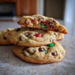 A stack of delicious Christmas Chocolate Chip Cookies, with a broken cookie on top revealing chocolate chips and festive M&Ms.