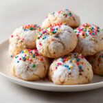 Pile of Christmas Funfetti Cake Mix Cookies on a white plate, dusted with powdered sugar and sprinkles.
