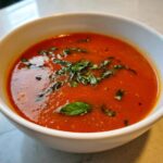 Close-up of a bowl of Classic Tomato Basil Soup, garnished with fresh basil.