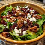A bowl of Cranberry Pecan Salad with Honey Dressing, featuring mixed greens, pecans, cranberries, and crumbled cheese.