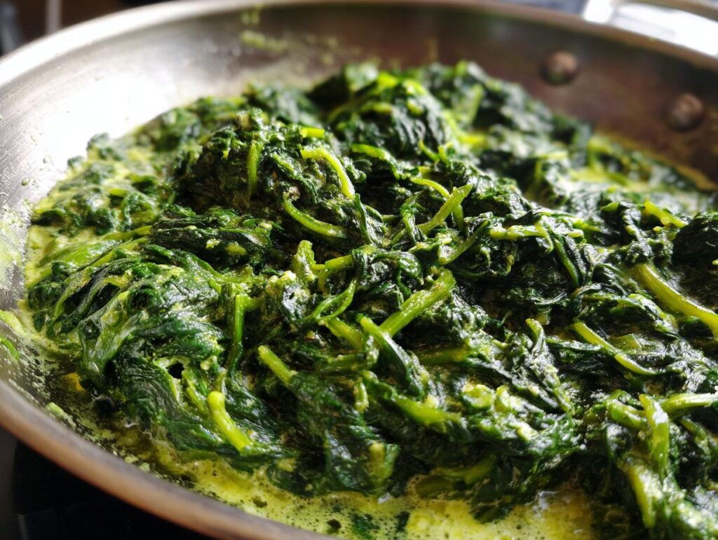 Close-up of Creamed Spinach cooking in a stainless steel pan, showing the creamy sauce and fresh spinach.