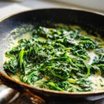 Close-up of Creamed Spinach cooking in a skillet, showing creamy sauce and fresh spinach.