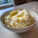 A bowl of creamy mashed potatoes topped with melted butter.