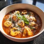 A bowl of Creamy Tomato Tortellini Soup garnished with basil and parmesan cheese.
