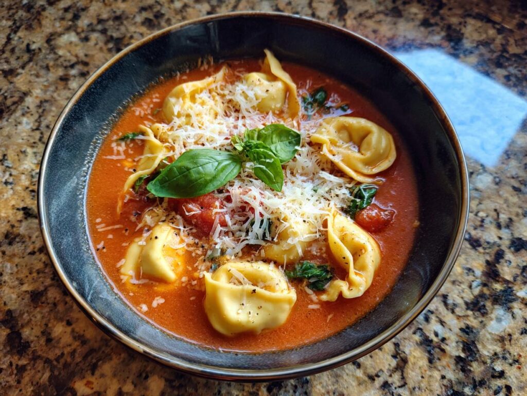 A bowl of Creamy Tomato Tortellini Soup, garnished with basil and parmesan cheese.
