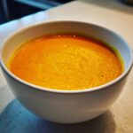 Close-up of a bowl of creamy Curried Cauliflower & Carrot Soup, a vibrant orange color.