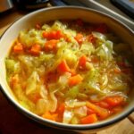 Close-up of a bowl filled with Detox Cabbage & Carrot Soup, featuring carrots and cabbage.