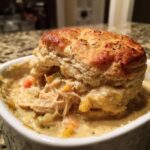 Close-up of an individual Flaky Biscuit Chicken Pot Pie in a white dish, with a golden biscuit topping.