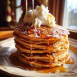 A stack of fluffy gingerbread pancakes drizzled with syrup and topped with whipped cream.