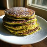 Stack of fluffy Green Smoothie Oatmeal Pancakes dusted with powdered sugar, on a white plate.