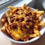 Close-up of a bowl of Hearty Chili Cheese Fries, with melted cheese and chili topping the fries.