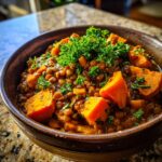 Close-up of a bowl of Hearty Lentil & Sweet Potato Stew, garnished with fresh herbs.