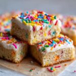 A stack of three Holiday Sugar Cookie Bars with Sprinkles, topped with white frosting and colorful sprinkles.