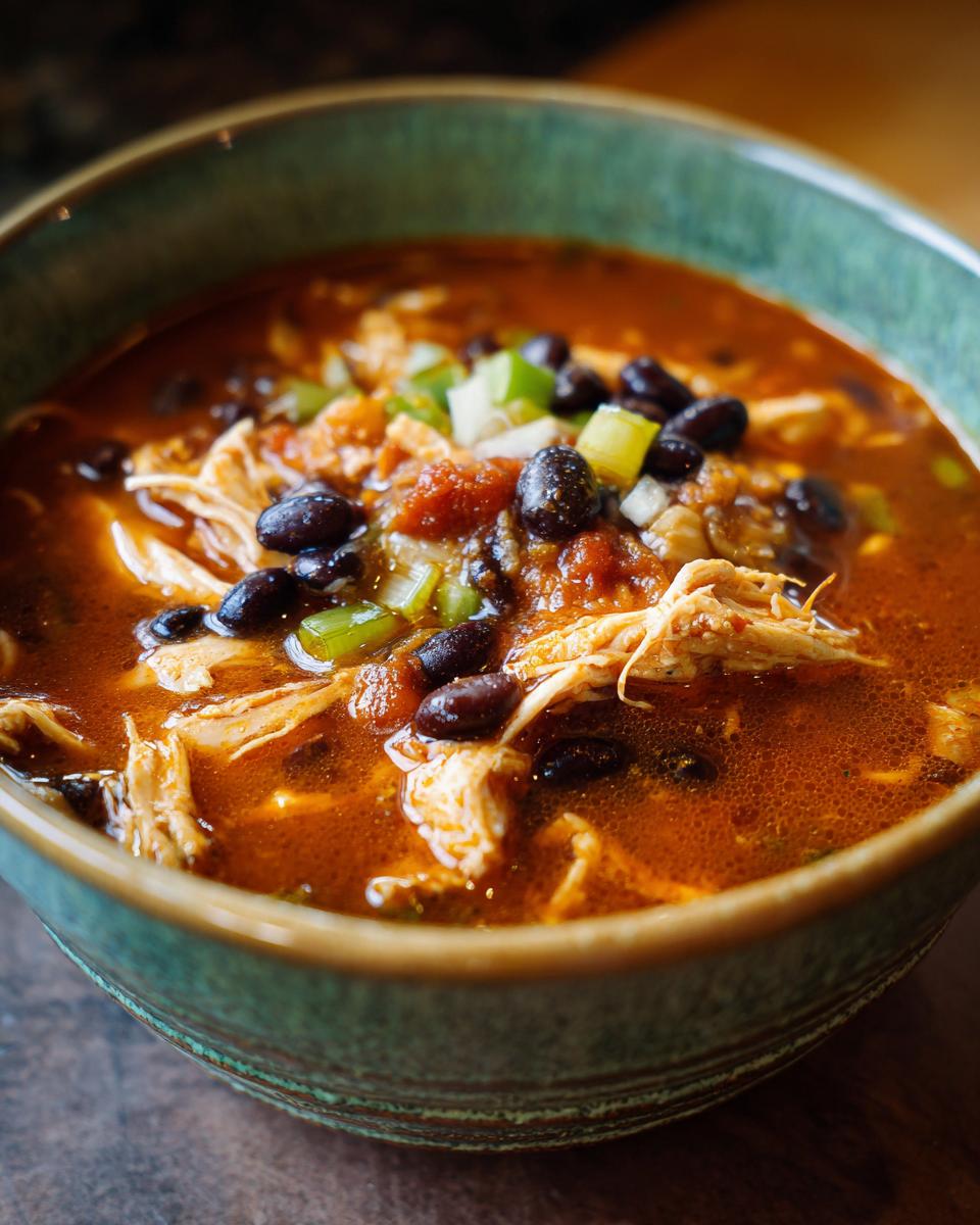 Close-up of a bowl of Instant Pot Chicken Enchilada Soup with chicken, black beans, and toppings.