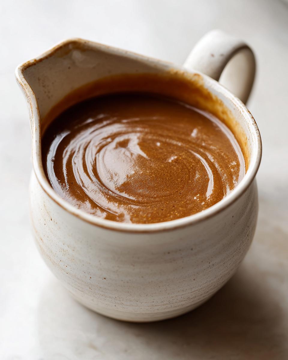 A close-up of rich, smooth Make-Ahead Thanksgiving Gravy served in a rustic ceramic gravy boat.