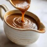 Close-up of rich, smooth Make-Ahead Thanksgiving Gravy being poured from a ladle into a rustic gravy boat.