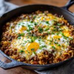 Close-up of a One-Pot Cheesy Beef and Rice Skillet with eggs, cheese, and herbs.