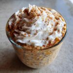 Close-up of a Pumpkin Spice Latte Overnight Oats in a glass, topped with whipped cream and cinnamon.