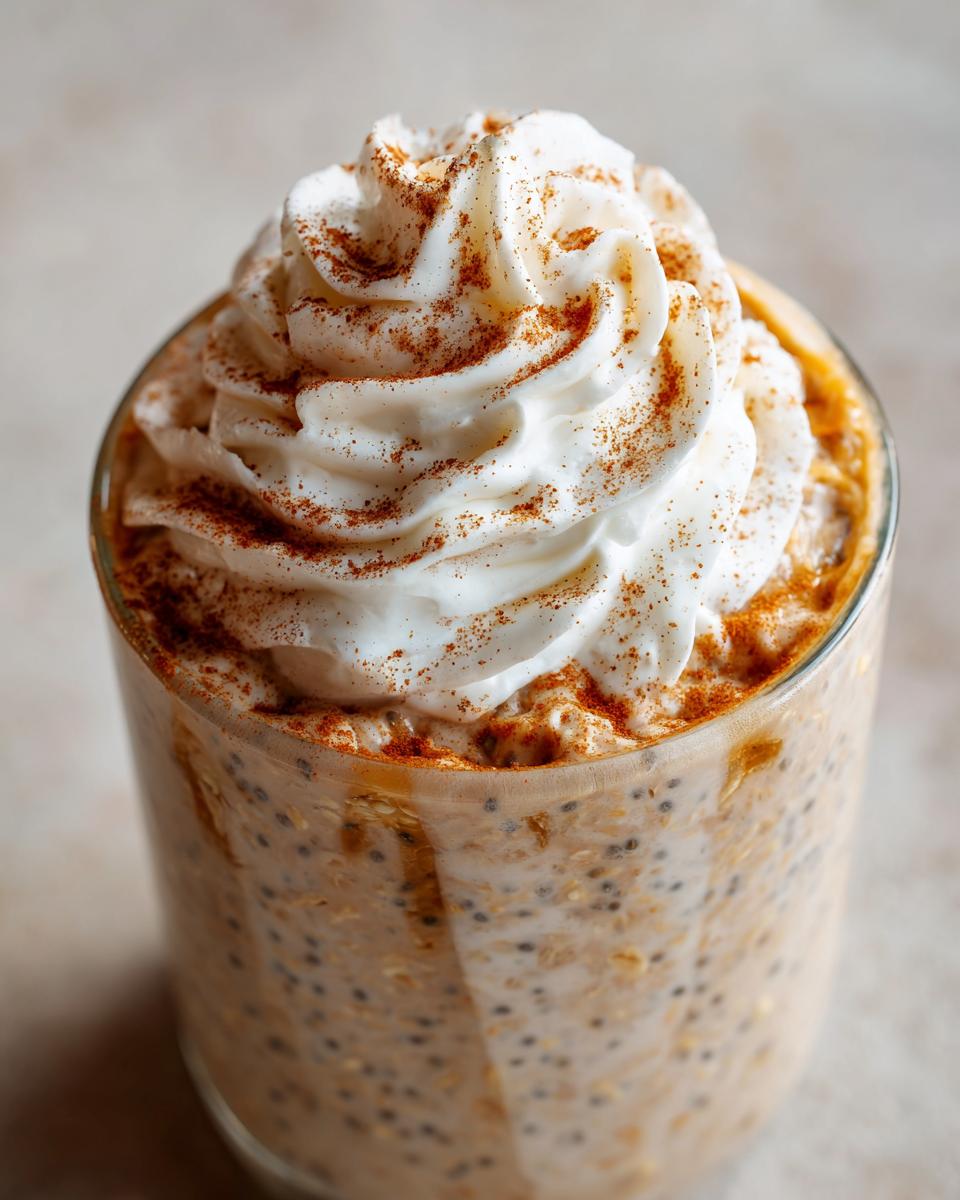 Close-up of a glass of Pumpkin Spice Latte Overnight Oats topped with whipped cream and cinnamon.