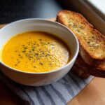 A bowl of creamy Roasted Butternut Squash Soup served with toasted bread, perfect for a cozy meal.