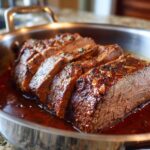 Close-up of sliced Rustic Red Wine Pot Roast in a stainless steel pan, showing tender meat and rich sauce.