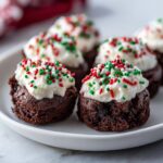 Close-up of Santa Hat Brownie Bites, chocolate brownies topped with white frosting and Christmas sprinkles.