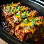 Close-up of Slow Cooker Bean and Cheese Enchiladas topped with cheese and green onions.