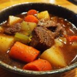 Close-up of a bowl of Slow Cooker Beef Stew Soup with beef chunks, carrots, potatoes, and celery.