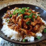 A bowl of white rice topped with shredded Slow Cooker Teriyaki Chicken and garnished with chopped green onions.