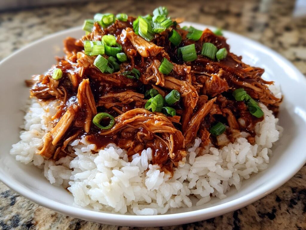 A bowl of fluffy white rice topped with shredded Slow Cooker Teriyaki Chicken and garnished with chopped green onions.