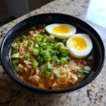 Close-up of a bowl of Spicy Ramen Noodle Soup with egg and green onions.