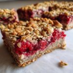 Close-up of a slice of Vegan Raspberry Chia Breakfast Bars with a raspberry filling and oat topping.