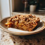 A close-up of a slice of warm apple crisp with a golden oat crumble topping, served on a plate.