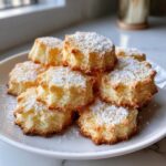 A pile of golden-brown whipped shortbread cookies dusted with powdered sugar on a white plate.