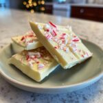 Close-up of three pieces of White Chocolate Peppermint Bark topped with crushed candy canes on a light green plate.