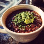 Close-up of a bowl of Zesty Black Bean Soup topped with avocado and fresh herbs.