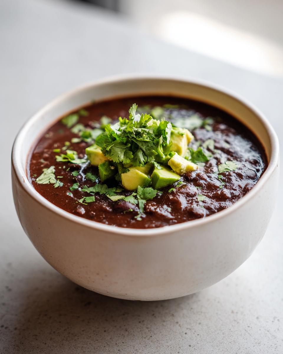 Close-up of a bowl of Zesty Black Bean Soup garnished with avocado and cilantro.