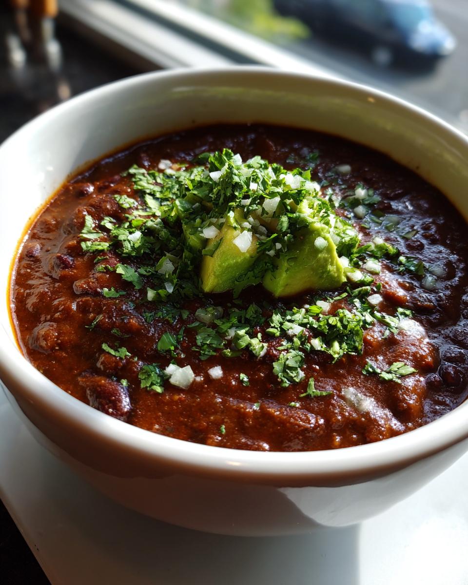 Close-up of a bowl of Zesty Black Bean Soup, topped with avocado, cilantro, and onions.